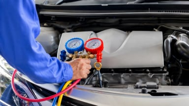 A technician using gauges on a car's AC system.