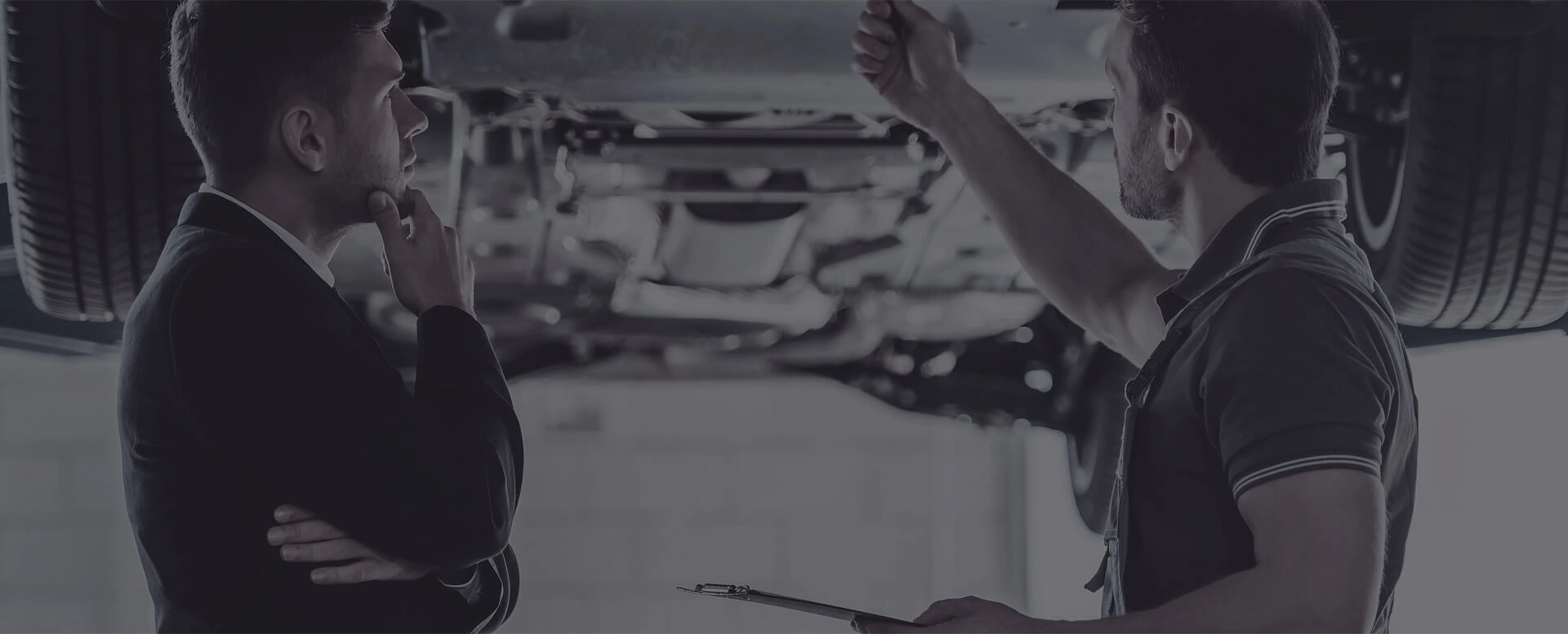 Two men discussing vehicle maintenance under a car
