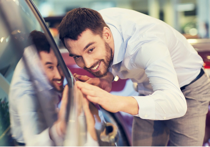 Man inspecting a car in a showroom, showcasing excitement.