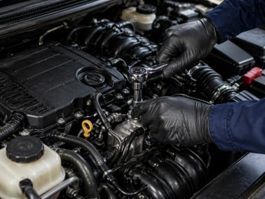 A mechanic using a wrench on a car engine.
